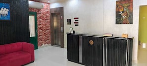 Una zona d'entrada amb un sofà vermell, un taulell de recepció negre, un ascensor i un quadre a la paret.