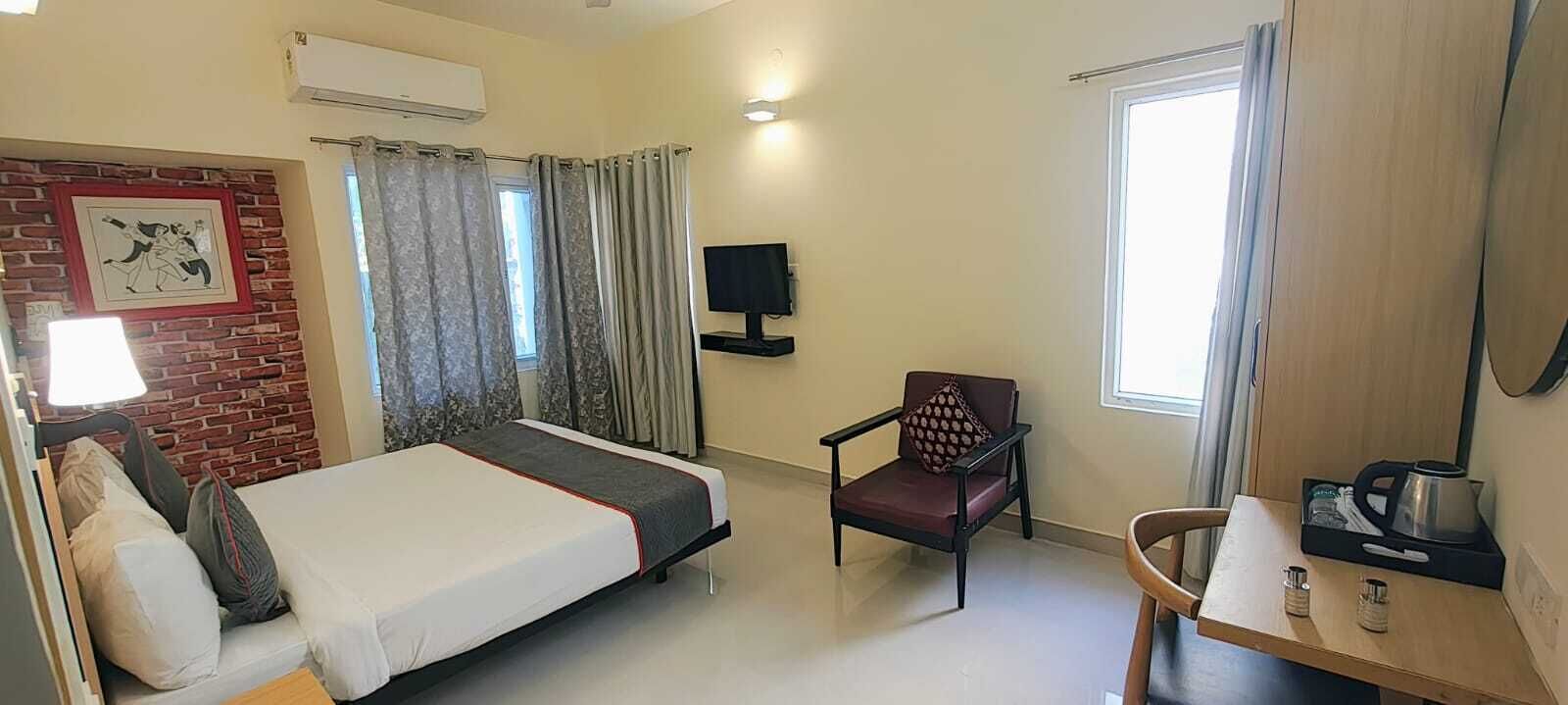 A hotel room with a bed, a chair, a desk with a tray, a TV, and a window with curtains.