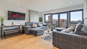 Una sala de estar moderna con un televisor de pantalla plana grande, sofás grises, una mesa de centro y una mesa de comedor con bancos.