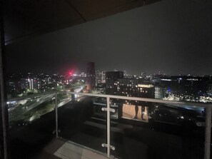 Une vue nocturne sur le paysage urbain, prise depuis un balcon doté d'une rambarde en verre.