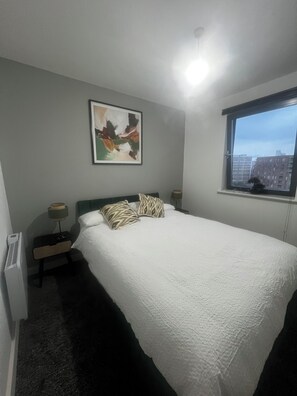 Une chambre à coucher avec un lit, une table de chevet, une lampe, une fenêtre donnant sur un beau paysage et un tableau accroché au mur.