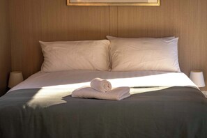 Un lit bien fait, avec une serviette pliée, deux lampes de chevet et un tableau encadré au-dessus du lit.