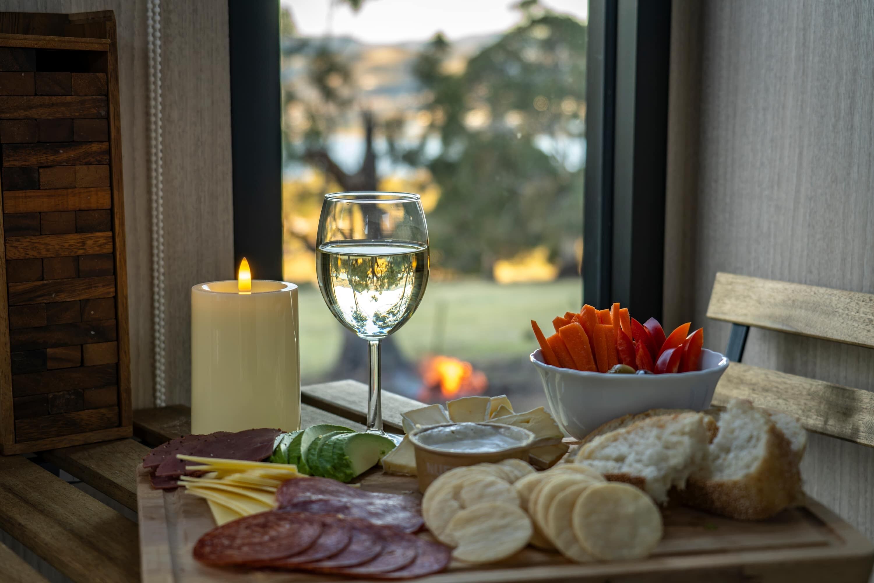 Uma mesa de madeira com diversos alimentos, uma vela e um copo de vinho branco.