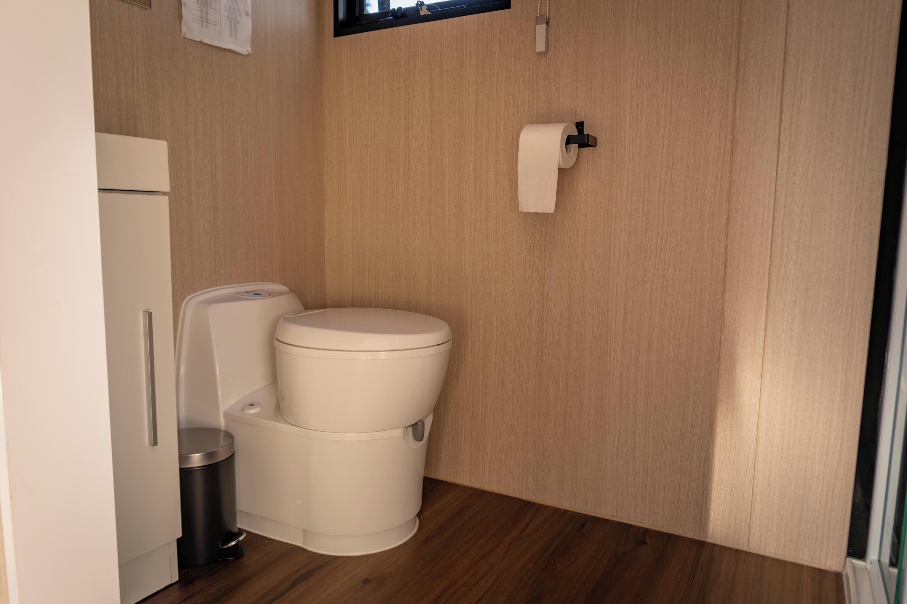 Ein kleines Badezimmer mit Toilette, Mülleimer und Toilettenpapierhalter an der Wand.