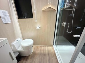 A modern bathroom with a toilet, a towel rack, a glass shower enclosure, and a wooden floor. - Black Snake Sky Box by Tiny Away (Granton)