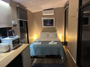 A hotel room with a bed, bedside lamps, a microwave, a coffee maker, and a painting on the wall. - Black Snake Sky Box by Tiny Away (Granton)