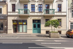 Ein Gebäude mit einer grünen Tür, auf der 'GARBARY 62' steht, einem kleinen Baum im Blumentopf und einem gelben Schild mit den Schriftzügen 'Idfast' und 'Powabimally KRP'.