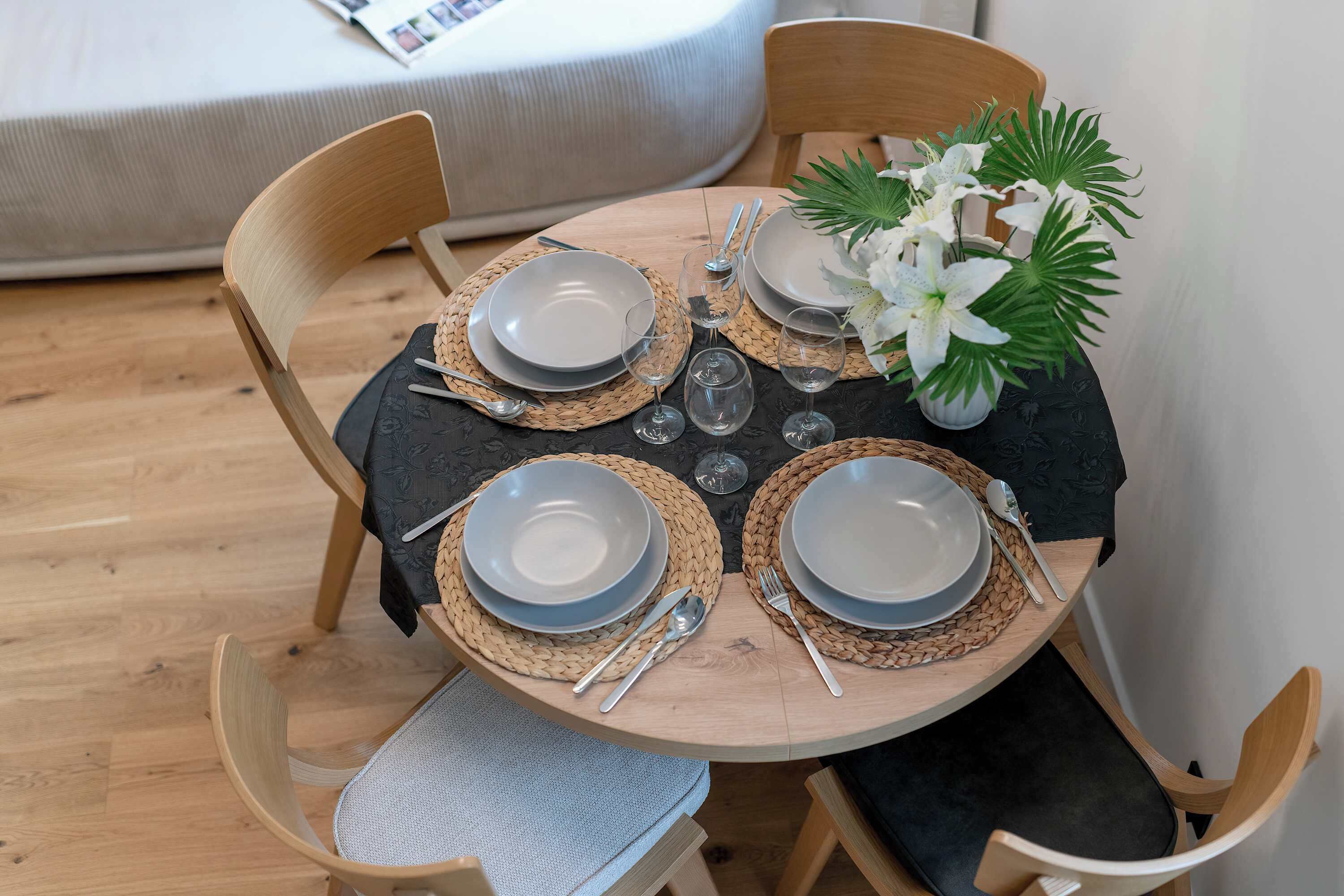 Une table de salle à manger ronde, avec quatre chaises, un vase de fleurs blanches et une nappe noire.