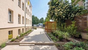 A pathway leading to a building with a yellow sign, a wooden pergola, and various plants. - Stylish Studio with a Mezzanine | Near the Market Square (Poznań)