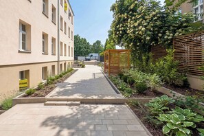 Ein Weg führt zu einem Gebäude mit einem gelben Schild, einer Holzpergola und verschiedenen Pflanzen.