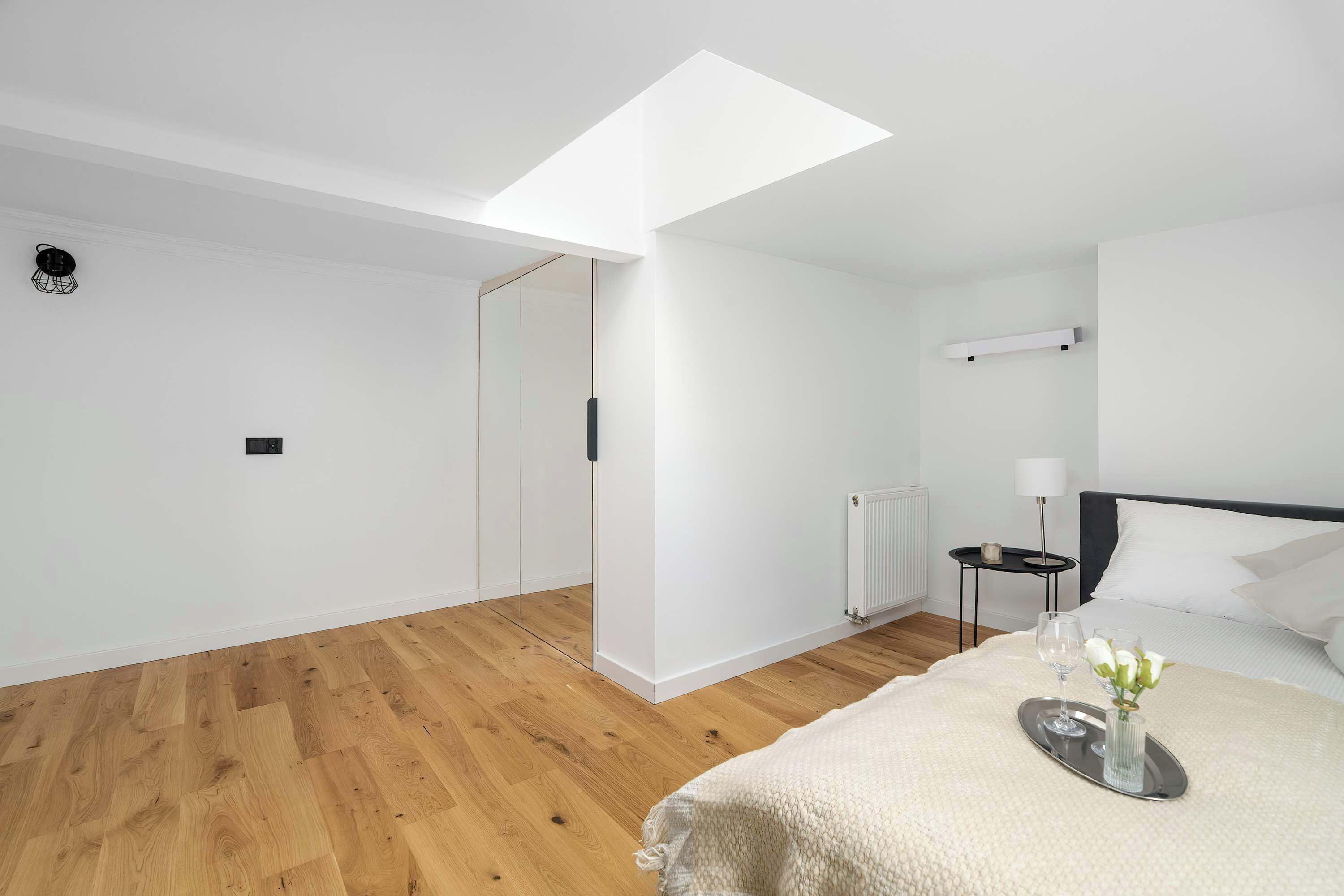 Una camera da letto moderna con un lucernario, un letto con un vassoio e fiori, un comodino e un termosifone.