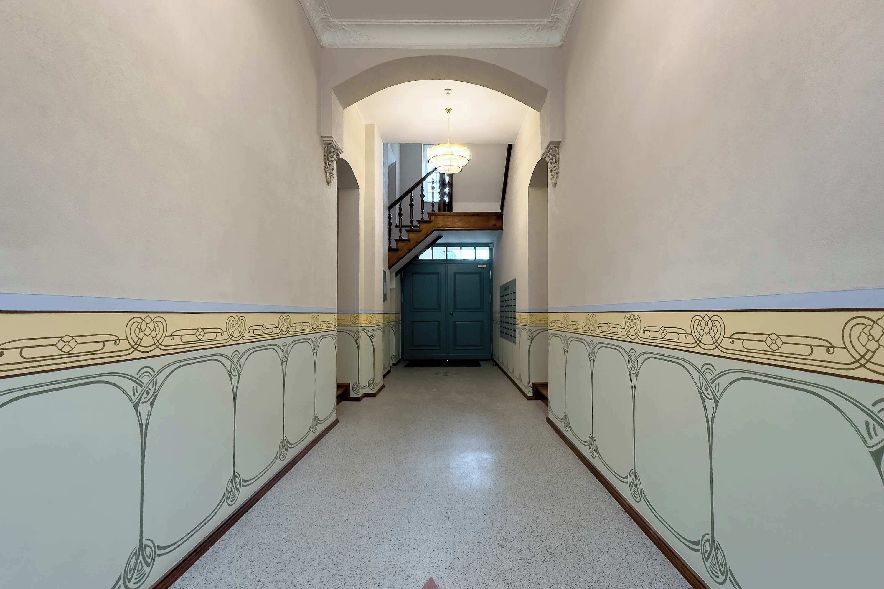 A hallway with ornate wall designs, a staircase, and a door.