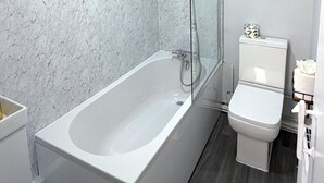 Een badkamer met een witte badkuip, een toilet en een marmeren wand.