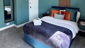 Een slaapkamer met een bed, een spiegel, een nachtkastje en een deur.