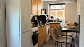 A compact kitchen with a refrigerator, oven, microwave, and washing machine. There is a small dining area with a table and chairs. - Central Hull, 3Br Contractors & Street Parking (Hull)