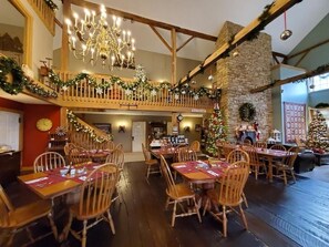 Zona pranzo con tavoli e sedie di legno, un lampadario e decorazioni natalizie.