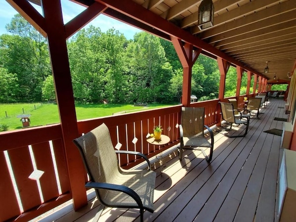 Une terrasse extérieure couverte, dotée de chaises et de tables, qui offre une vue sur un paysage verdoyant.