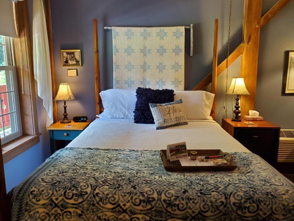 Un letto con una coperta a motivi, un cuscino con scritte, un vassoio con vari oggetti e una parete decorata con un arazzo decorativo.