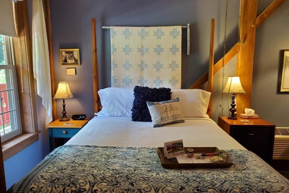 A bed with a patterned bedspread, a pillow with text, a tray with items, and a wall with a patterned tapestry.