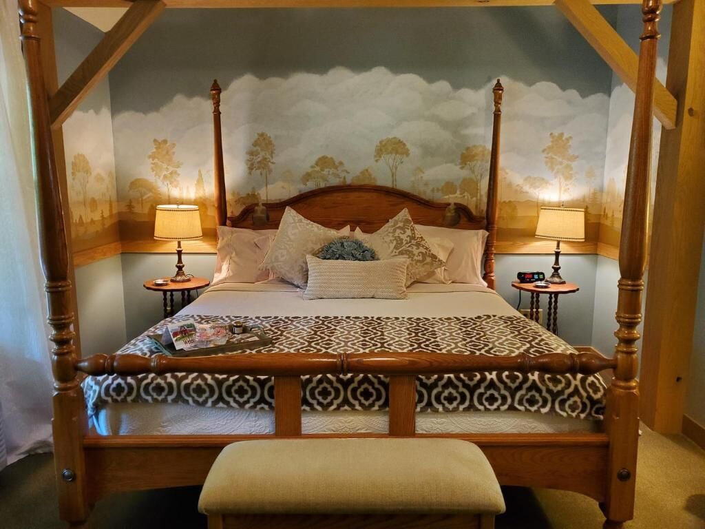 Un letto a baldacchino con una coperta a motivi, due lampade da comodino e un affresco sulla parete.