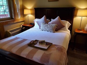 A neatly made bed with pillows, a bedside table with a lamp, and a tray with a welcome card. - The Barn Inn Bed and Breakfast (Millersburg)