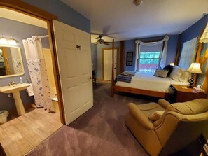 Una camera da letto con un letto, una sedia, un comodino, una lampada, una finestra e un bagno con lavandino e specchio.
