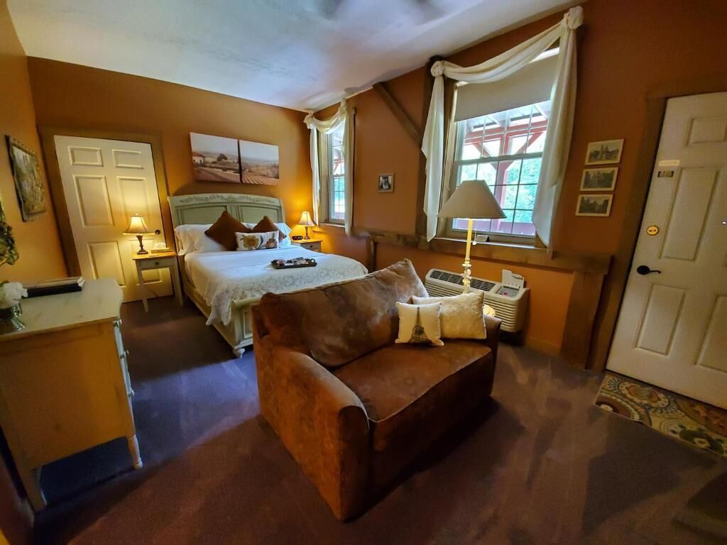 Una camera da letto con un letto, comodini, un divano, una finestra con tende, un termosifone e una porta.