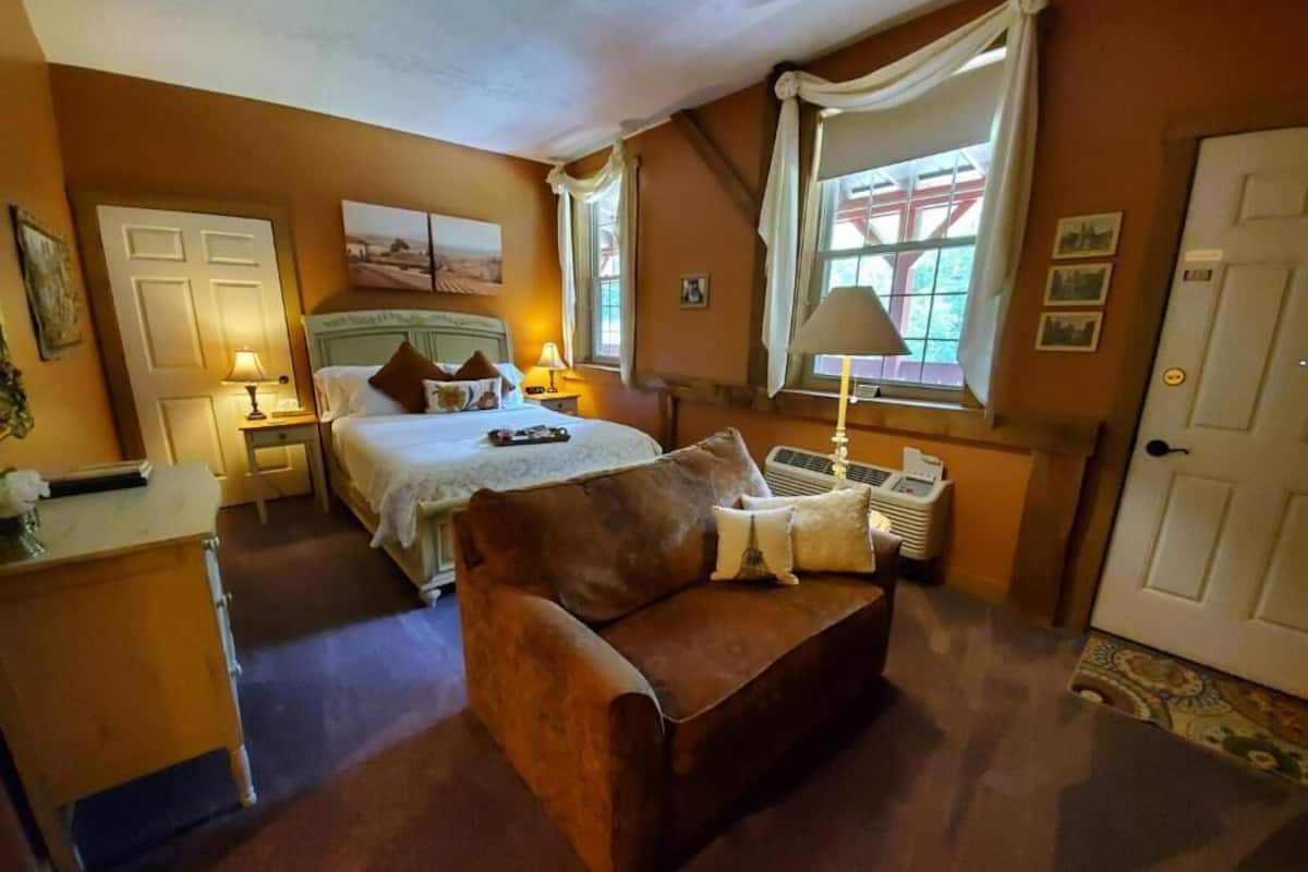 A bedroom with a bed, bedside tables, a sofa, a window with curtains, a radiator, and a door.