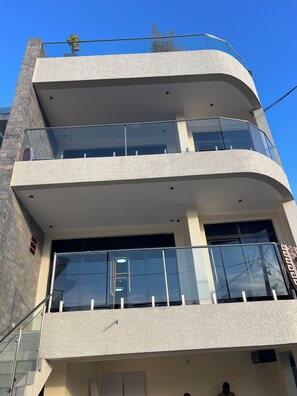 Um edifício de vários andares com arquitetura moderna, com varandas e guarda-corpos de vidro e fachada texturizada.