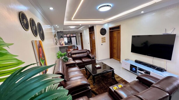 A modern living room with leather sofas, a flat-screen TV, and a dining area in the background. - Adorable 2-bedroom bed & breakfast in vibrant Kigali (Kigali)