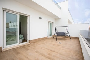 Ein Balkon mit einer Schaukel, Glastüren und Blick auf Gebäude.