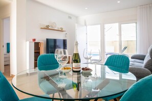 Uma sala de estar moderna com uma mesa de jantar de vidro, cadeiras verde-água, uma televisão e uma janela grande.
