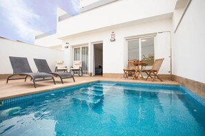 Piscina com espreguiçadeiras e uma mesa, porta de correr de vidro e um aviso de alarme visível.