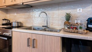 A kitchen with a stainless steel sink, wooden cabinets, a built-in oven, and a countertop with a basket of fruits and a pineapple. - Elysium Villanova Apartment Near Airport (Rhodes)