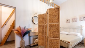 A bedroom with a bed, a bedside table, a mirror, a woven partition, a vase with feathers, and a staircase. - Elysium Villanova Apartment Near Airport (Rhodes)