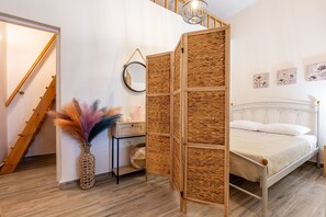 A bedroom with a bed, a bedside table, a mirror, a woven partition, a vase with feathers, and a staircase.