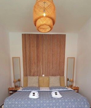 A hotel room with a bed, two bedside lamps, a large mirror, a wooden slat wall, and a hanging light fixture. - Acropolis View Apartment in Heart of Monastiraki (Athina)
