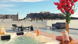 A rooftop terrace with a hot tub, lounge chairs, and a view of ancient ruins. - Acropolis View Apartment in Heart of Monastiraki (Athina)