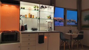 A modern kitchen with a built-in oven, a glass-fronted shelving unit with jars and plants, a sink, and a dining area with two chairs. - Acropolis View Apartment in Heart of Monastiraki (Athina)