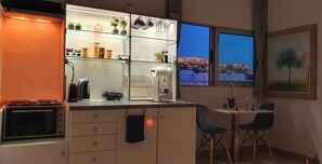 A modern kitchen with a built-in oven, a glass-fronted shelving unit with jars and plants, a sink, and a dining area with two chairs. - Acropolis View Apartment in Heart of Monastiraki (Athina)