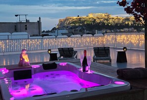 Een dakterras met een jacuzzi, lounge fauteuils en uitzicht op een historisch gebouw.