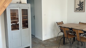 Una zona de menjador amb taula i cadires de fusta, un moble amb portes de vidre i una porta que condueix a una altra habitació.