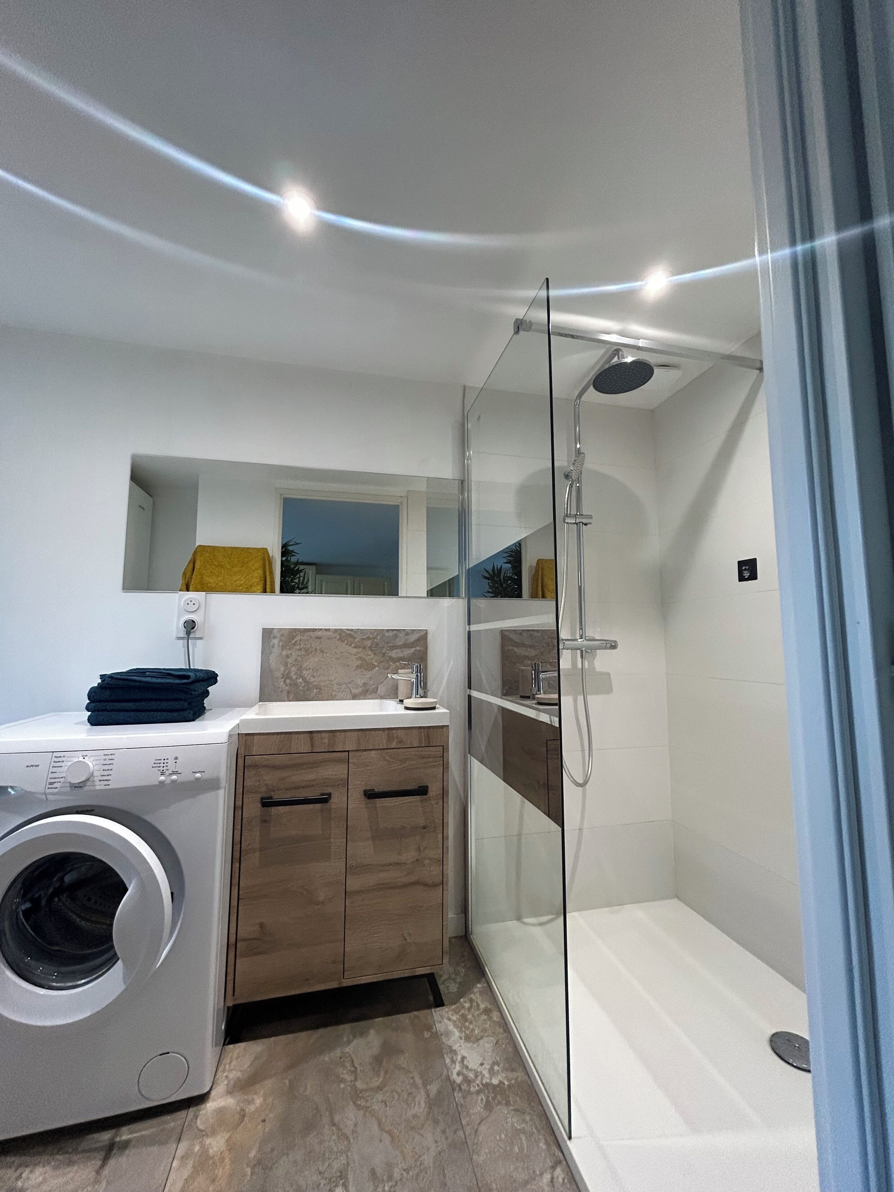 Een moderne badkamer met een douchecabine van glas, een wasmachine en een wastafel met spiegel.