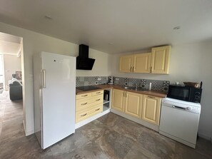 A kitchen with a refrigerator, microwave, dishwasher, and wooden cabinets. - La Petite Maison (Toutlemonde)