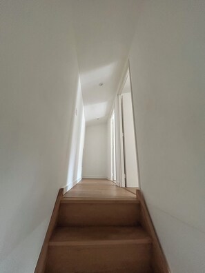 A narrow, well-lit hallway with wooden steps leading to a door. - La Petite Maison (Toutlemonde)