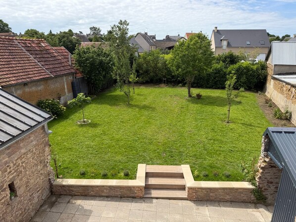 A residential backyard with a grassy lawn, a small tree, and a stone staircase leading to a raised platform. - Vrbo Property (Périers)