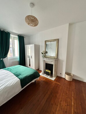 A bedroom with a bed, a fireplace, a mirror, and a window with curtains. - Vrbo Property (Périers)