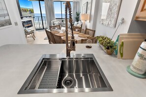 A modern kitchen with a stainless steel sink, wicker furniture, and a view of the beach. - Spinnaker #304 - Beautiful Oceanfront Condo in North Myrtle Beach (North Myrtle Beach)
