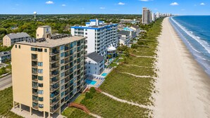 A coastal hotel with multiple floors, a swimming pool, and a beach view.