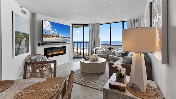 A modern living room with a fireplace, a television, and a view of the beach.